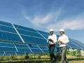 Deux hommes en casque blanc inspectent un champ de panneaux solaires, discutant d'un bail emphytéotique photovoltaïque sous un ciel bleu.