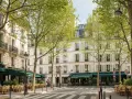 Rue parisienne bordée d'arbres feuillus, immeubles haussmanniens, terrasses de café. Un décor idéal pour rêver à comment acheter un appartement.