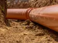 Gros plan sur une canalisation orange dans une tranchée. La servitude de canalisation enterrée est en cours d'installation, prête à être recouverte de terre.