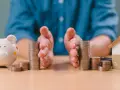 Mains protégeant des piles de pièces, symbolisant la gestion financière et la **desolidarisation pret immo**. Une tirelire et une maison miniature sont visibles.