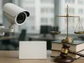 Caméra de surveillance, balance de la justice et marteau d'avocat sur un bureau. La jurisprudence en matière de caméra surveillance travail est complexe.