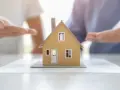 Modèle de maison sur des documents, mains en arrière-plan suggérant une solution pour sortir de l'indivision sans vendre.