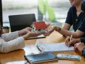 Une maison miniature est remise, un contrat est signé, et de l'argent est posé sur la table, suggérant une transaction immobilière et un chèque de caution.