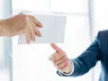Main d'un homme en costume remettant une enveloppe blanche à une autre main. Peut-être une mise en demeure URSSAF avec un délai de paiement.