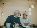 Couple âgé discutant de la différence entre article 82 et 83, l'un écrit, l'autre utilise une calculatrice.
