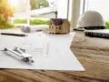 Plans, maquette de maison, casque et ordinateur sur un bureau en bois. La question est : combien de temps est valable un permis de construire ?