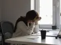 Une personne accablée par la pression au travail, la tête entre les mains, assise à un bureau encombré.