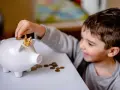 Un garçon met une pièce dans une tirelire en forme de cochon couronné. Une leçon précoce sur la fiscalité PEL à 12 ans.