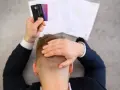 Homme stressé tenant des cartes bancaires, face à des documents. Il pense à l'effacement des dettes et aux loyers impayés.