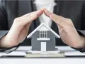 Mains protégeant une maquette de maison, symbolisant la **garantie de bon fonctionnement** et la sécurité de votre investissement immobilier.