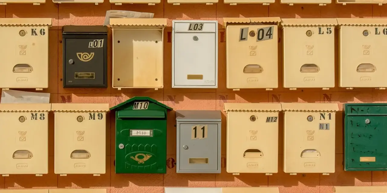 Rangées de boîtes aux lettres de copropriété, certaines jaunes, une verte, une noire et une blanche, avec des numéros et des symboles.