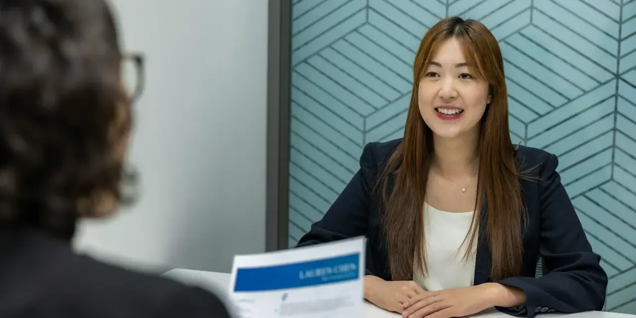 Une femme souriante en entretien, son CV sur la table. Elle semble confiante, peut-être reçoit-elle une lettre de recadrage positive pour un nouveau poste.