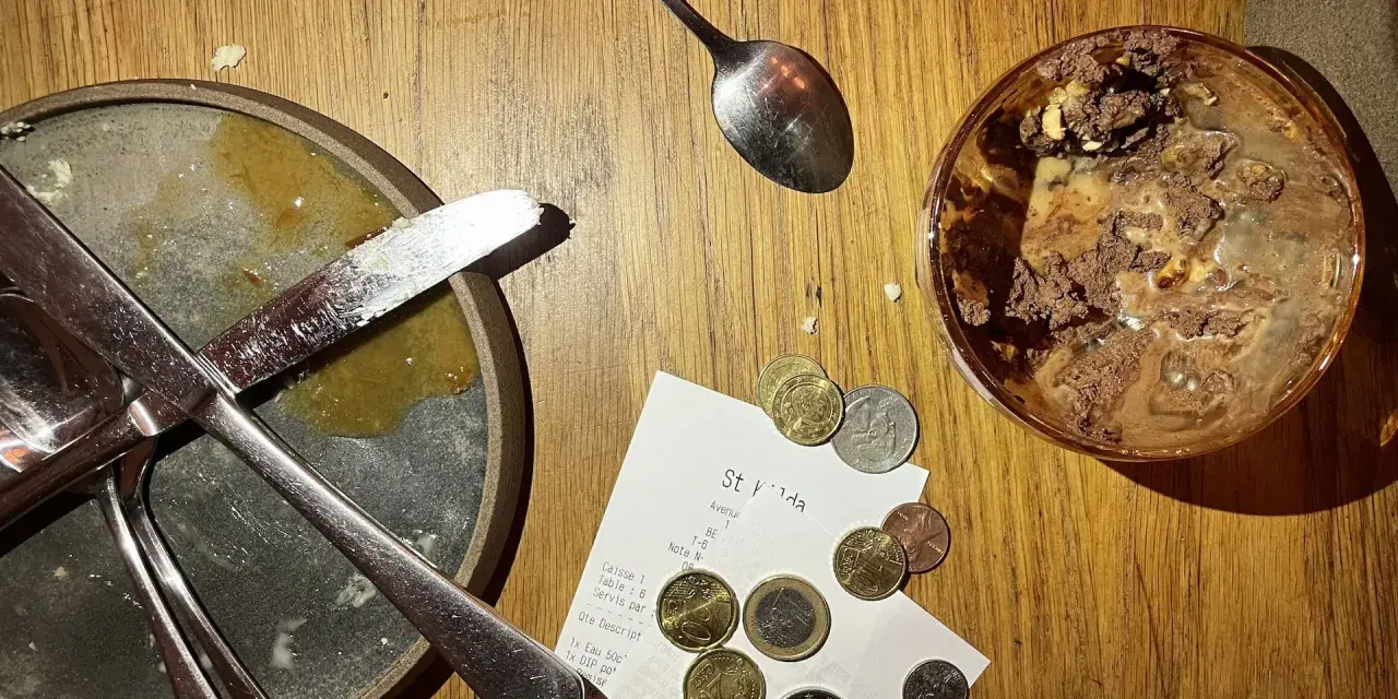 Sur une table en bois, un reçu et des pièces de monnaie sont posés près d'une assiette sale et d'un verre de dessert. Le patron peut-il garder les pourboires ?