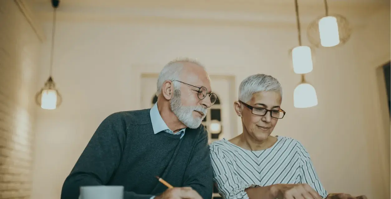 Couple âgé discutant de la différence entre article 82 et 83, l'un écrit, l'autre utilise une calculatrice.