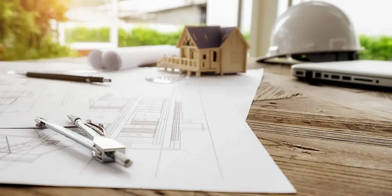 Plans, maquette de maison, casque et ordinateur sur un bureau en bois. La question est : combien de temps est valable un permis de construire ?