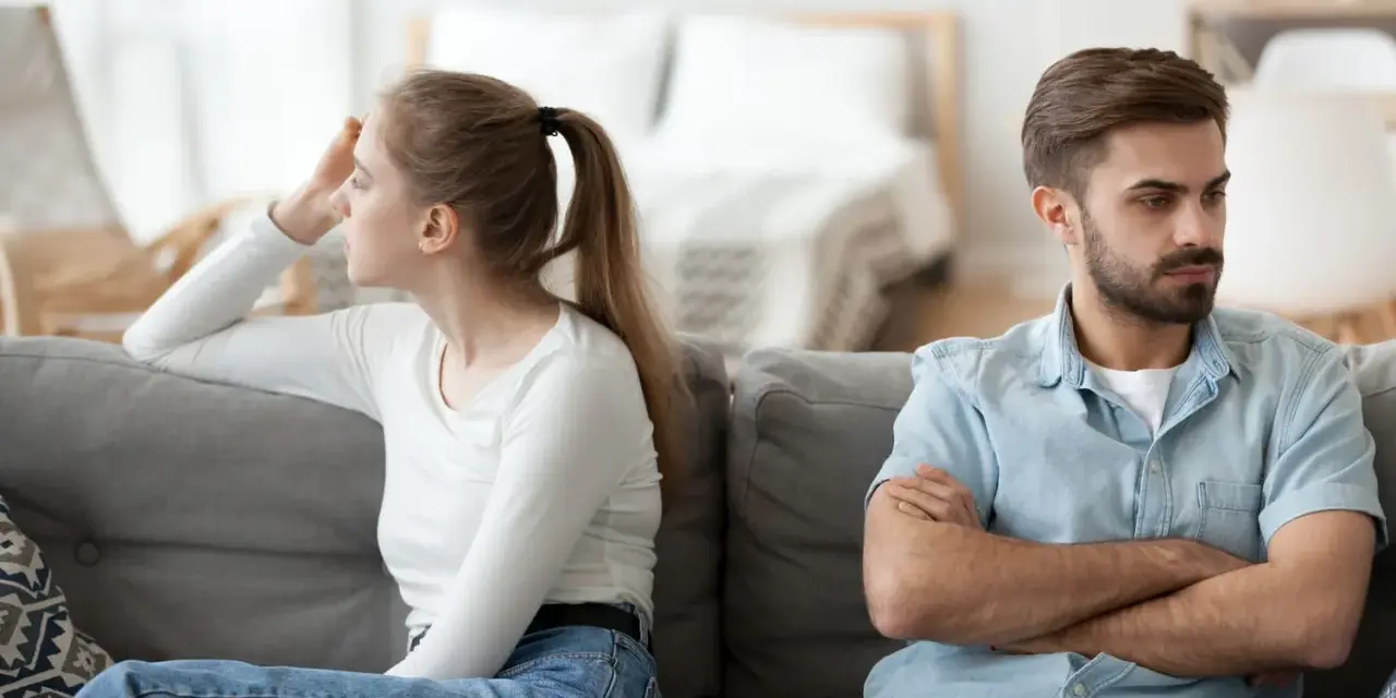 Couple marié, domicile différent, impôt. Ils sont assis sur un canapé, dos à dos, visiblement en désaccord.