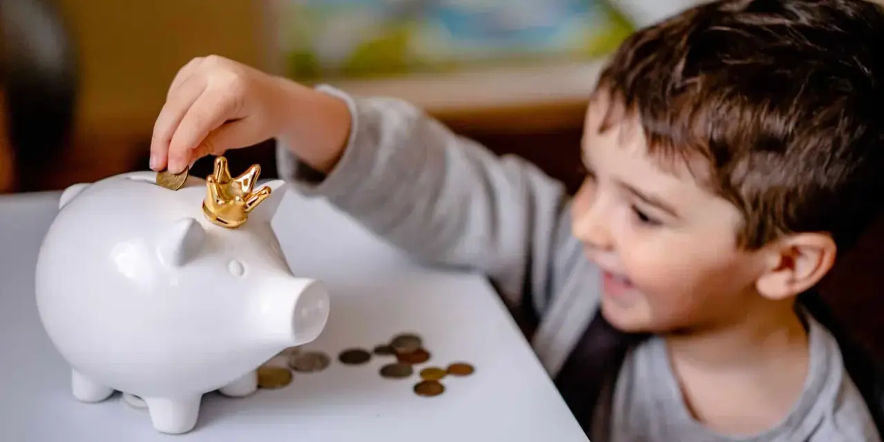 Un garçon met une pièce dans une tirelire en forme de cochon couronné. Une leçon précoce sur la fiscalité PEL à 12 ans.