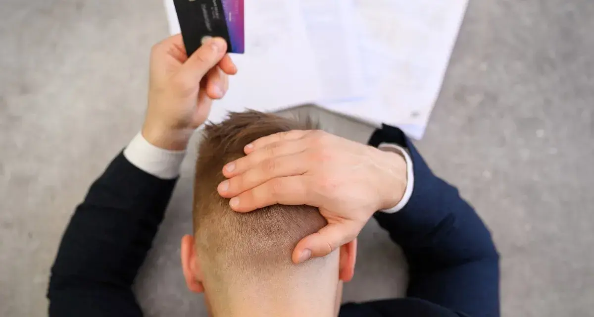 Homme stressé tenant des cartes bancaires, face à des documents. Il pense à l'effacement des dettes et aux loyers impayés.