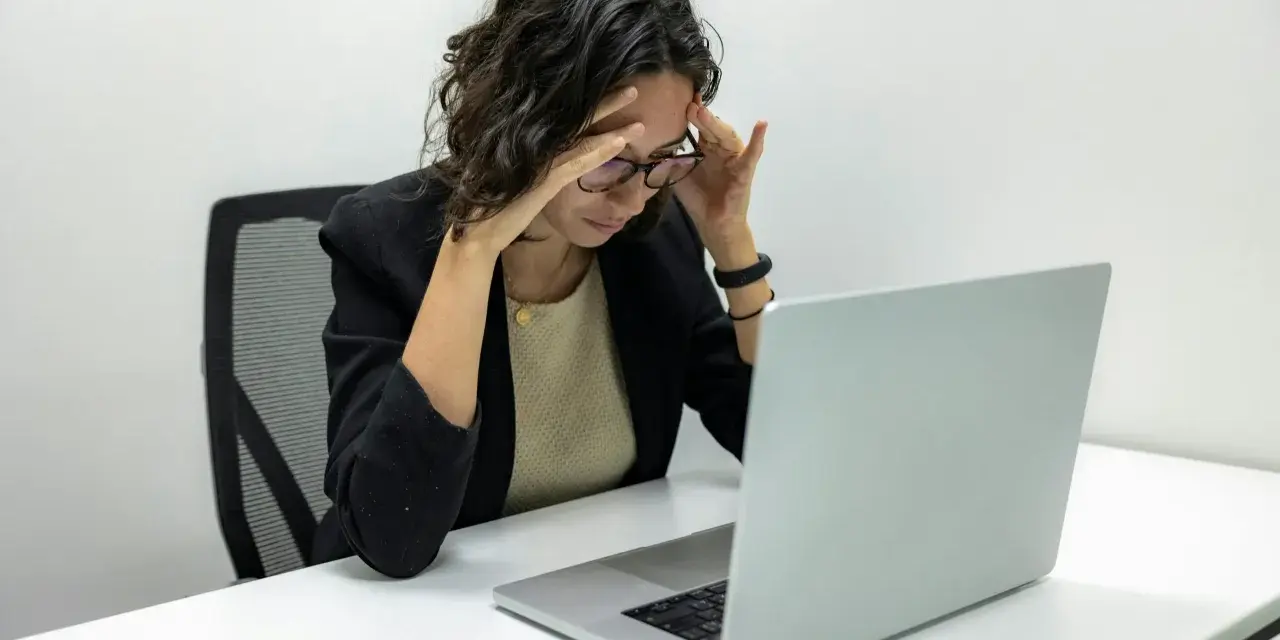 Femme stressée devant son ordinateur, les mains sur les tempes. Une situation difficile, peut-être un licenciement pendant arrêt maladie pour dépression.