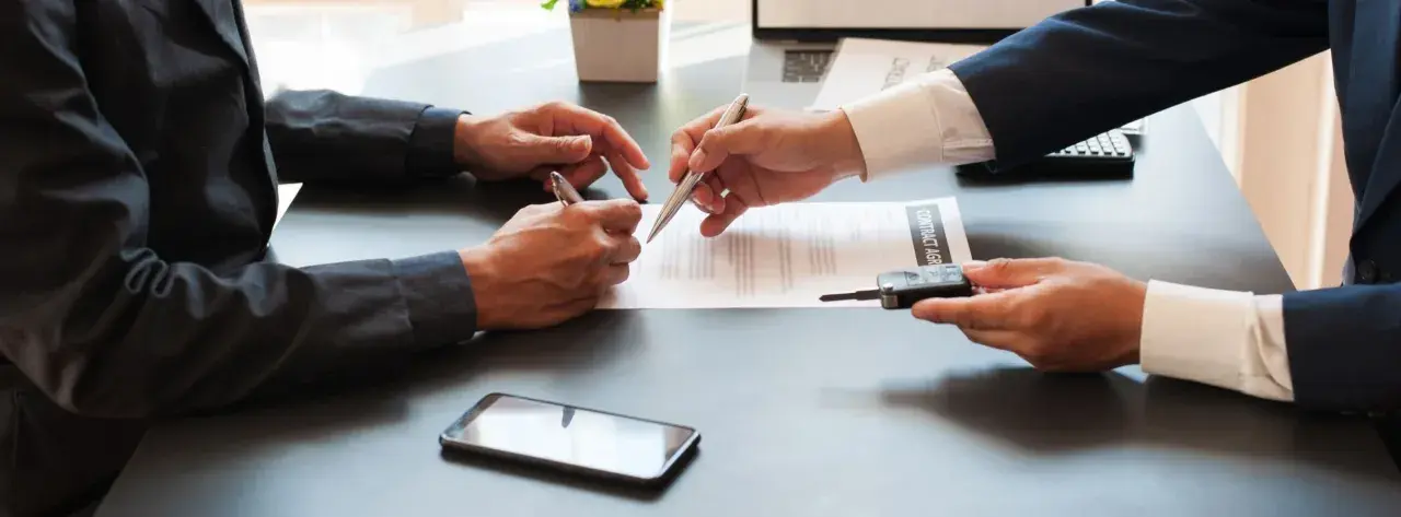Deux hommes signent un contrat, l'un remettant les clés d'un véhicule. Une transaction pour un **gapd bail commercial** est en cours.