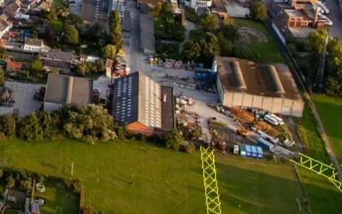 Vue aérienne d'un lotissement et d'une zone industrielle. Un pylône jaune est visible, marquant un emplacement réservé pour le droit de délaissement.
