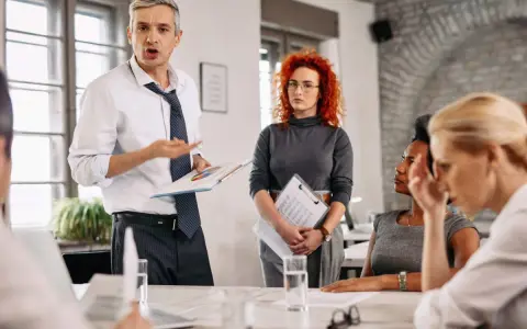 Un homme présente un rapport du liquidateur à une équipe. Une femme aux cheveux roux écoute attentivement.