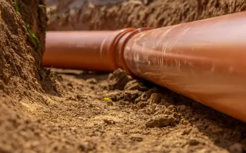 Gros plan sur une canalisation orange dans une tranchée. La servitude de canalisation enterrée est en cours d'installation, prête à être recouverte de terre.