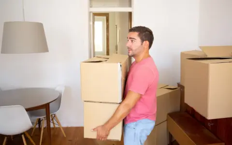 Un homme porte des cartons, prêt à quitter le domicile conjugal. Le propriétaire semble pensif, entouré de cartons de déménagement.