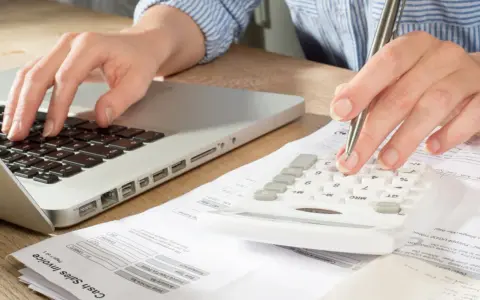 Main tenant calcule son solde de tout compte imposable sur une calculatrice, un ordinateur et des factures.