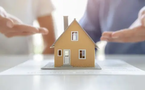 Modèle de maison sur des documents, mains en arrière-plan suggérant une solution pour sortir de l'indivision sans vendre.