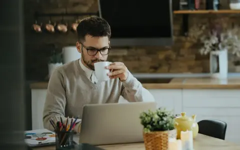Homme buvant un café devant son ordinateur, pensant à son indemnité transactionnelle CSG CRDS.