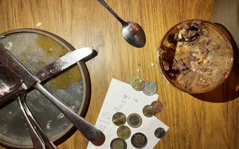 Sur une table en bois, un reçu et des pièces de monnaie sont posés près d'une assiette sale et d'un verre de dessert. Le patron peut-il garder les pourboires ?