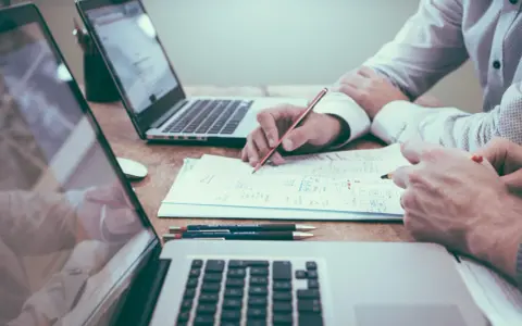 Deux personnes travaillent sur des documents et des ordinateurs portables, discutant du droit de la mode.