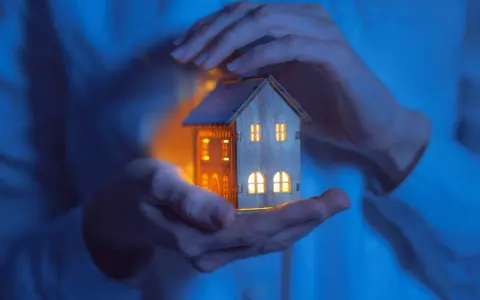Mains tenant une maisonnette illuminée, symbolisant la jurisprudence logement de fonction et la protection du foyer.