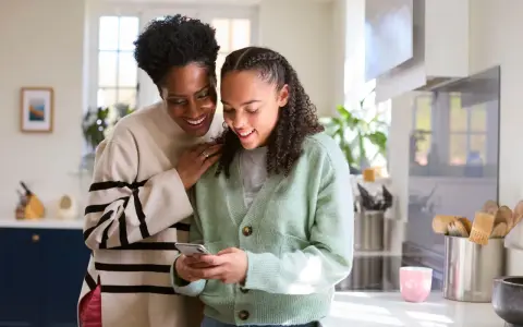 Mère et fille souriantes regardant un téléphone. Une conversation sur la pension alimentaire jusqu'à quel âge.