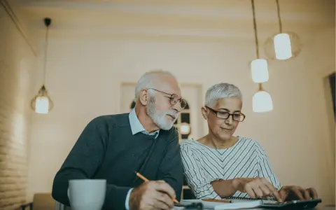 Couple âgé discutant de la différence entre article 82 et 83, l'un écrit, l'autre utilise une calculatrice.