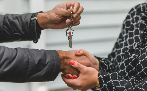 Une main tend une clé avec un porte-clés en forme de maison. Les deux mains se serrent, symbolisant la fin d'une obligation de relogement par la mairie.