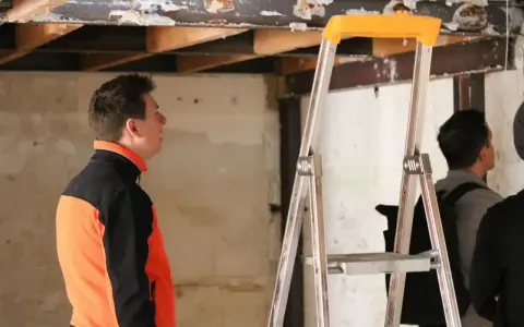Un homme en veste orange et noire observe le plafond délabré d'un chantier. L'architecte assure le suivi de chantier, une obligation pour garantir la qualité des travaux.