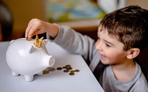 Un garçon met une pièce dans une tirelire en forme de cochon couronné. Une leçon précoce sur la fiscalité PEL à 12 ans.