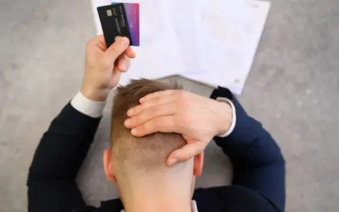 Homme stressé tenant des cartes bancaires, face à des documents. Il pense à l'effacement des dettes et aux loyers impayés.