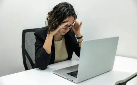 Femme stressée devant son ordinateur, les mains sur les tempes. Une situation difficile, peut-être un licenciement pendant arrêt maladie pour dépression.