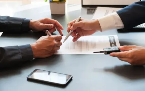 Deux hommes signent un contrat, l'un remettant les clés d'un véhicule. Une transaction pour un **gapd bail commercial** est en cours.