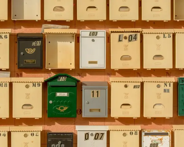 Rangées de boîtes aux lettres de copropriété, certaines jaunes, une verte, une noire et une blanche, avec des numéros et des symboles.