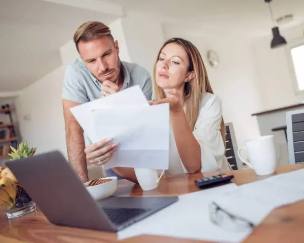 Couple discutent de documents, peut-être une pacs déclaration séparée, devant un ordinateur portable.