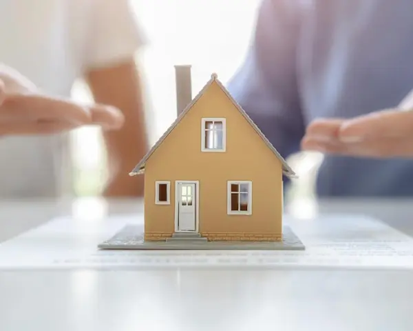Modèle de maison sur des documents, mains en arrière-plan suggérant une solution pour sortir de l'indivision sans vendre.