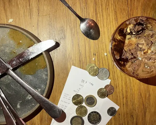 Sur une table en bois, un reçu et des pièces de monnaie sont posés près d'une assiette sale et d'un verre de dessert. Le patron peut-il garder les pourboires ?