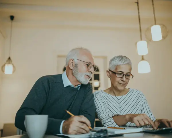 Couple âgé discutant de la différence entre article 82 et 83, l'un écrit, l'autre utilise une calculatrice.
