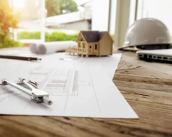 Plans, maquette de maison, casque et ordinateur sur un bureau en bois. La question est : combien de temps est valable un permis de construire ?