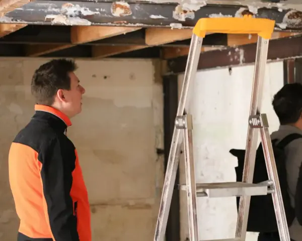 Un homme en veste orange et noire observe le plafond délabré d'un chantier. L'architecte assure le suivi de chantier, une obligation pour garantir la qualité des travaux.