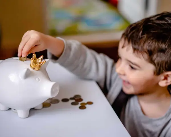 Un garçon met une pièce dans une tirelire en forme de cochon couronné. Une leçon précoce sur la fiscalité PEL à 12 ans.